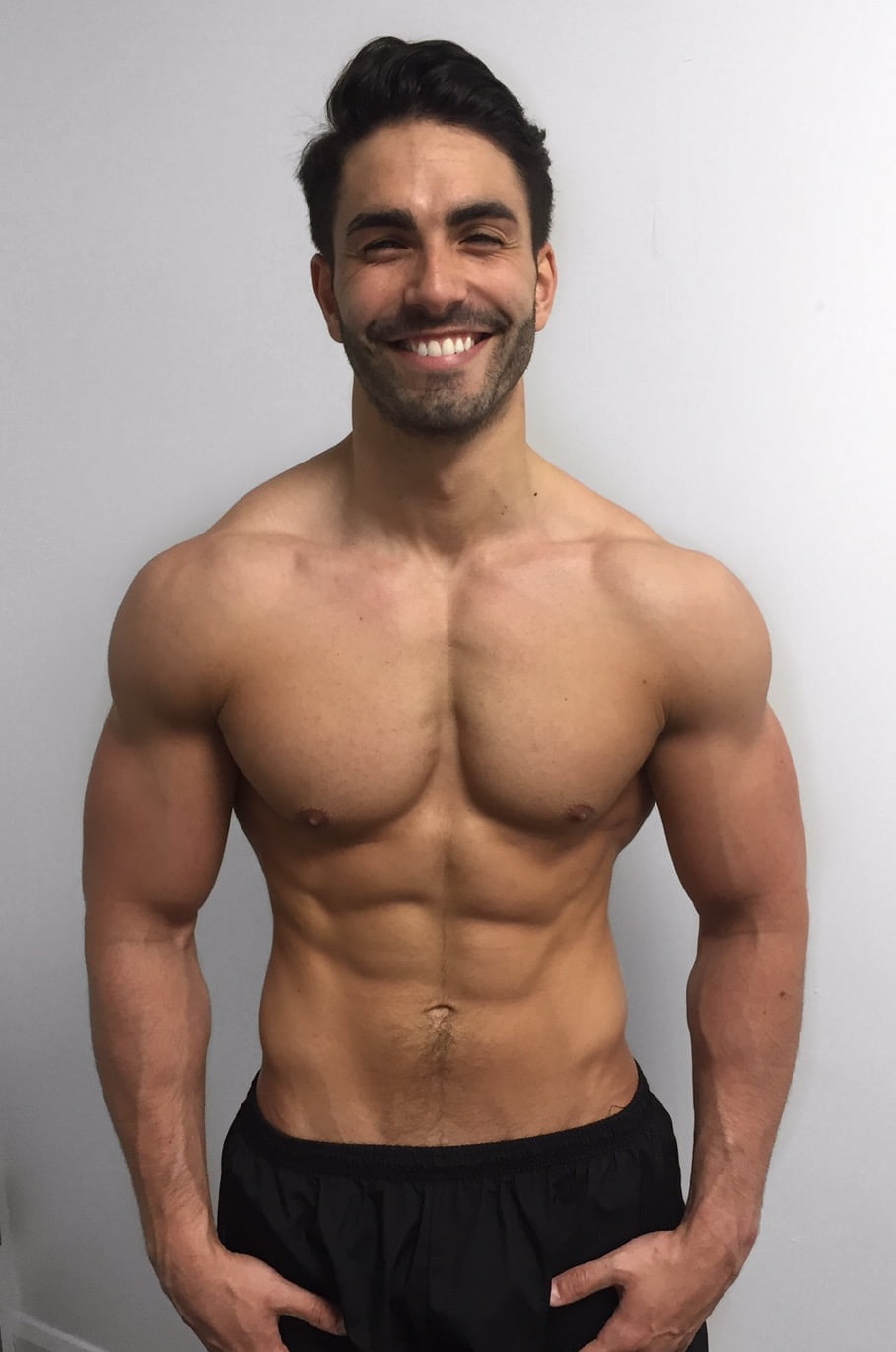 A man after his fitness transformation, standing against a white background, showcasing a muscular and toned physique.