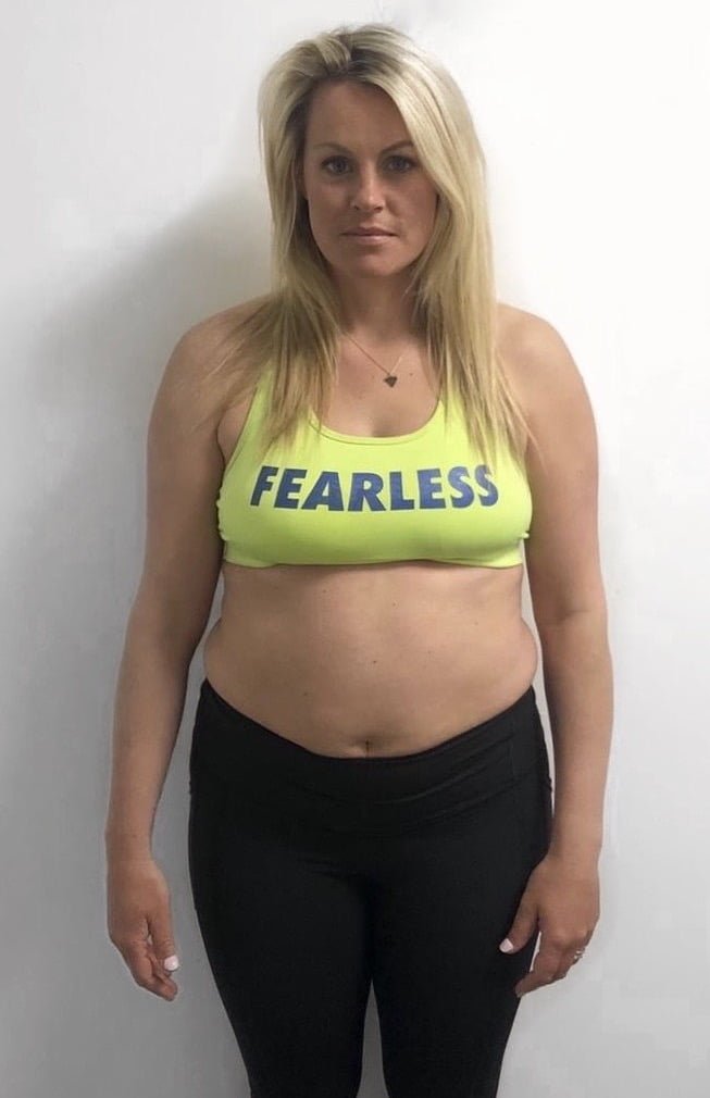 A woman before her fitness transformation, wearing a yellow sports bra and standing against a white background, showcasing her initial physique.