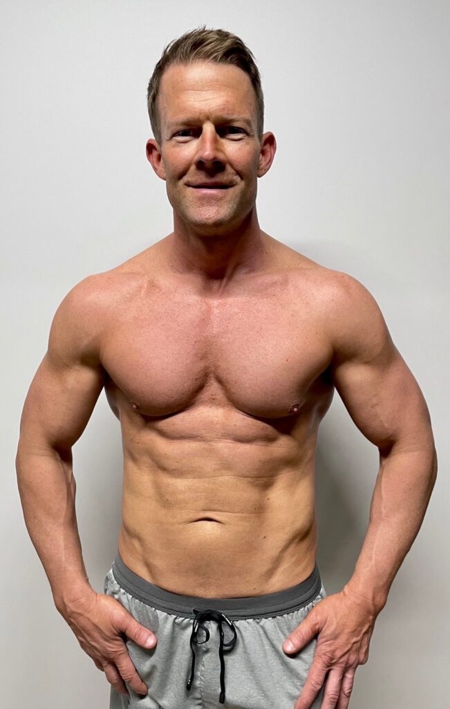 A man after his fitness transformation, standing against a white background, showcasing a toned and muscular physique.