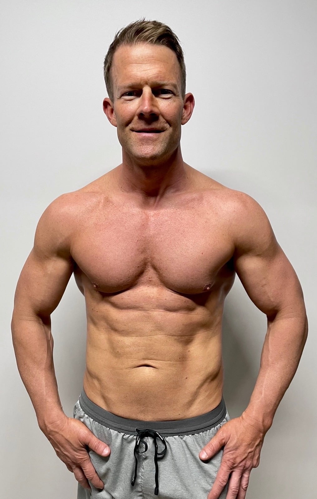 A man after his fitness transformation, standing against a white background, showcasing a toned and muscular physique.