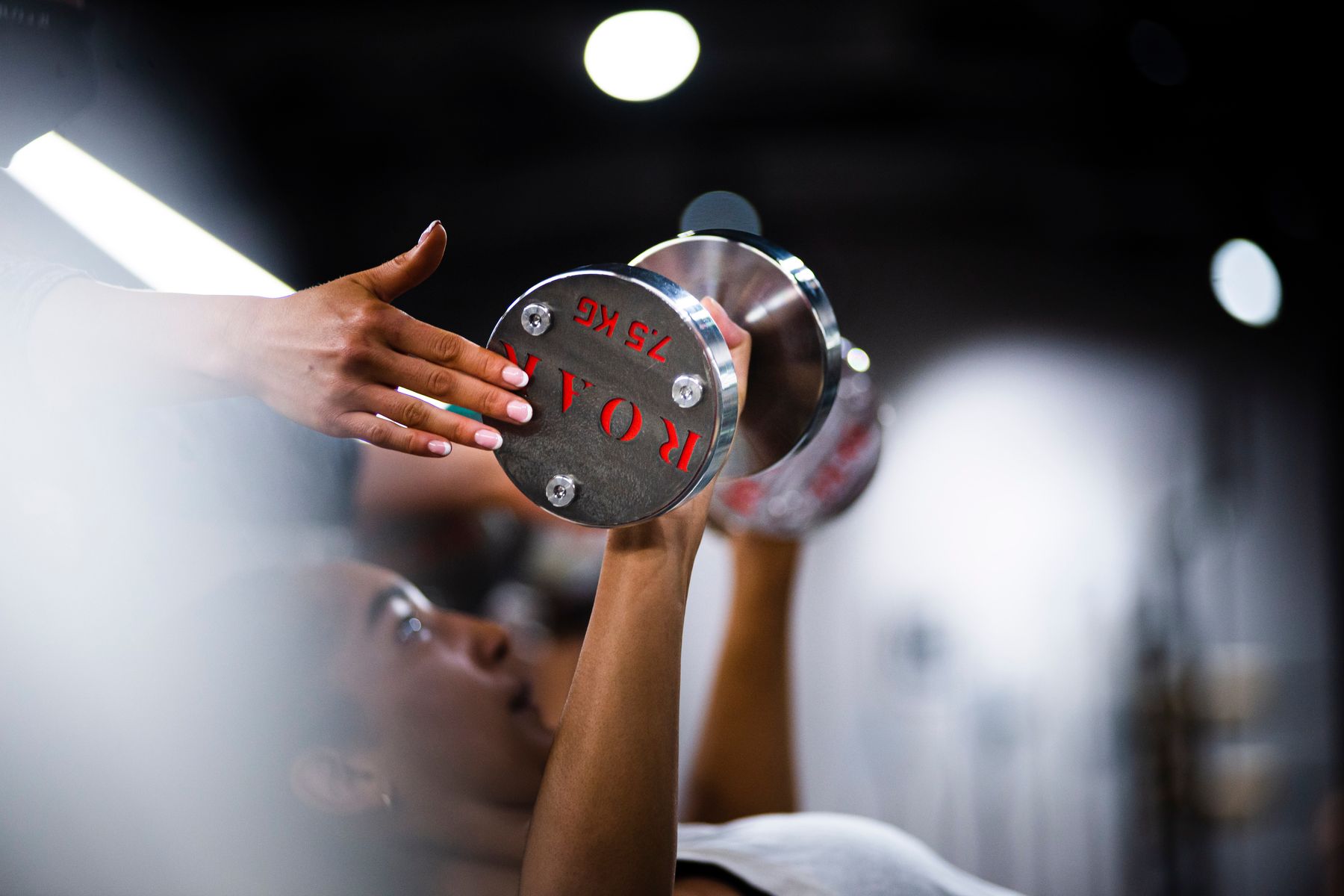 Personal trainer spotting a client during a dumbbell press with ROAR dumbbells