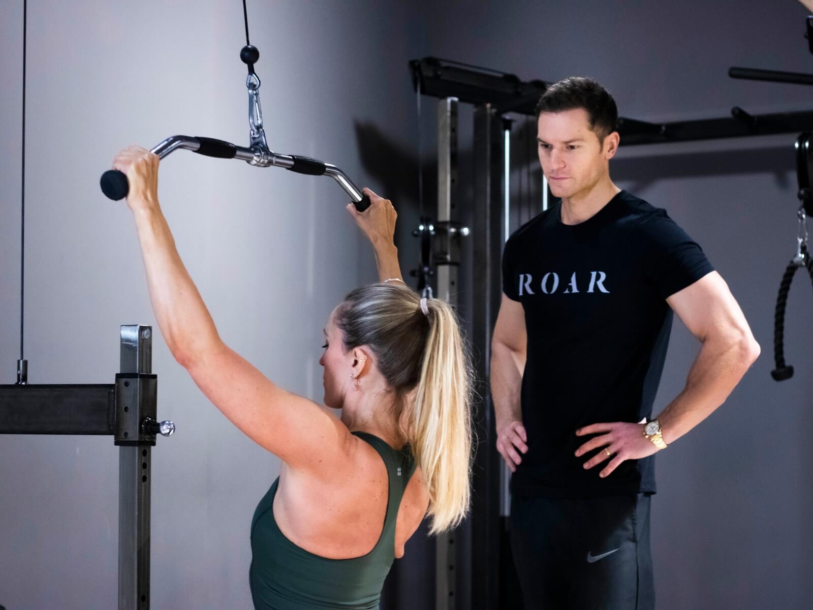 Roar Fitness personal trainer Rich Phillips coaching a client through a cable lat pulldown in the gym